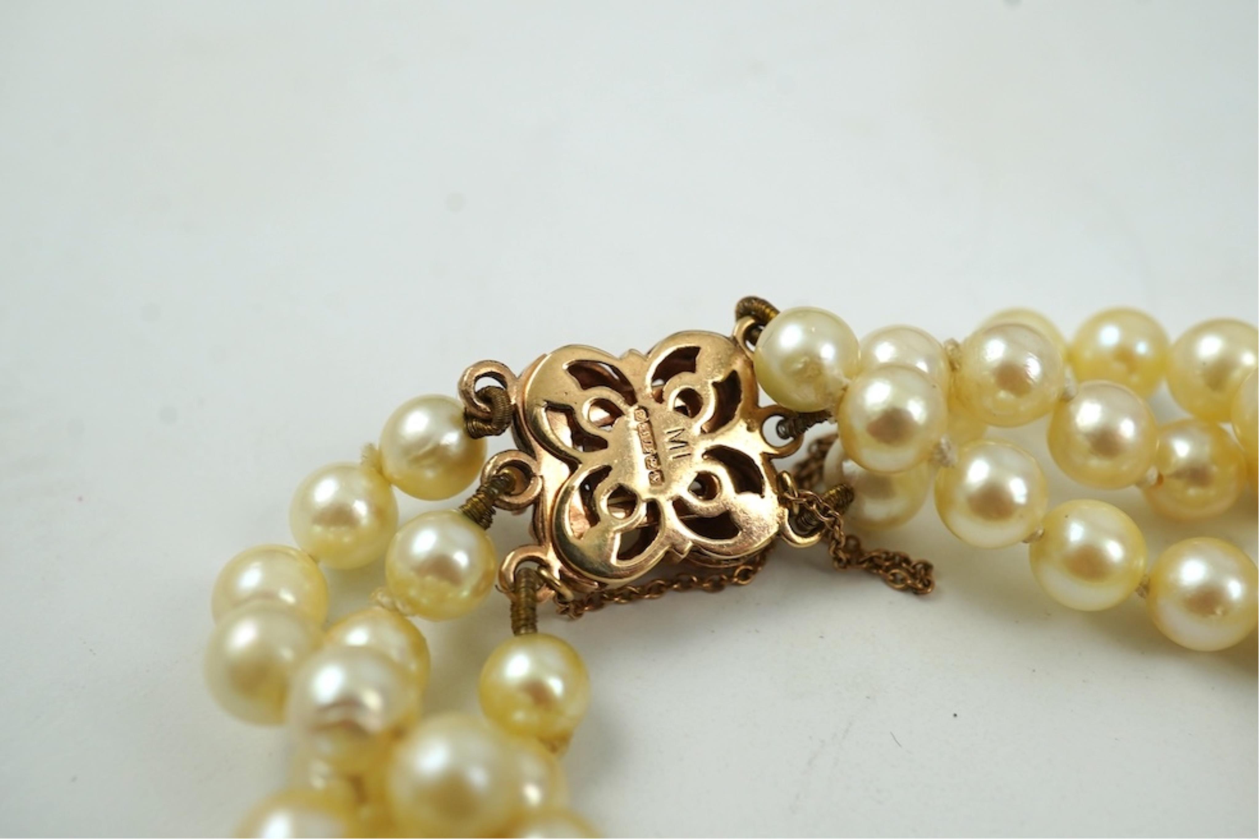 A triple strand cultured pearl bracelet, with a 9ct gold, garnet and cultured pearl cluster set clasp, 16cm.